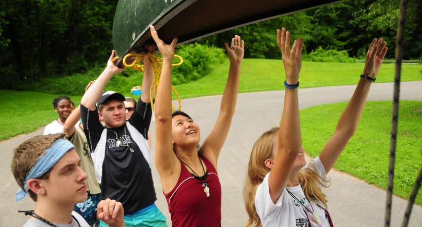 A group of students lift a canoe above their heads